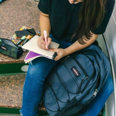Scholier met Eastpak rugzak op de trap die wat in haar agenda schrijft.